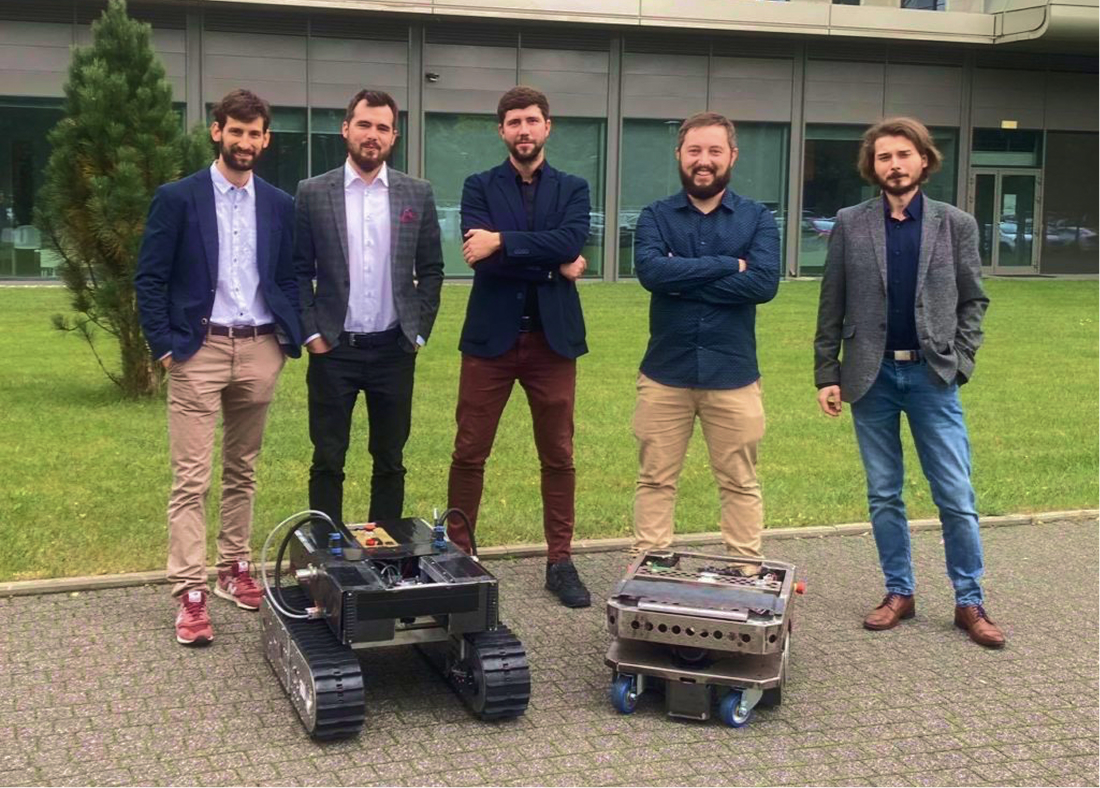 Zespół Hetbot pozujący na zewnątrz z dwoma robotami mobilnymi przed budynkiem